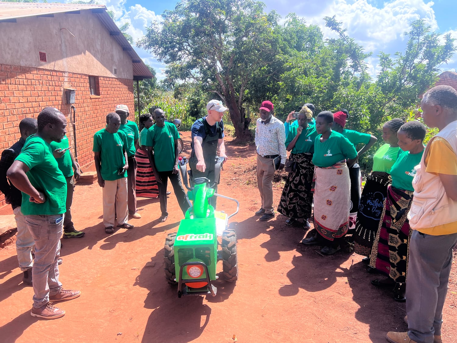 A community group in green Aftrak shirts standing with the AFT-e1 outside a brick building in Malawi